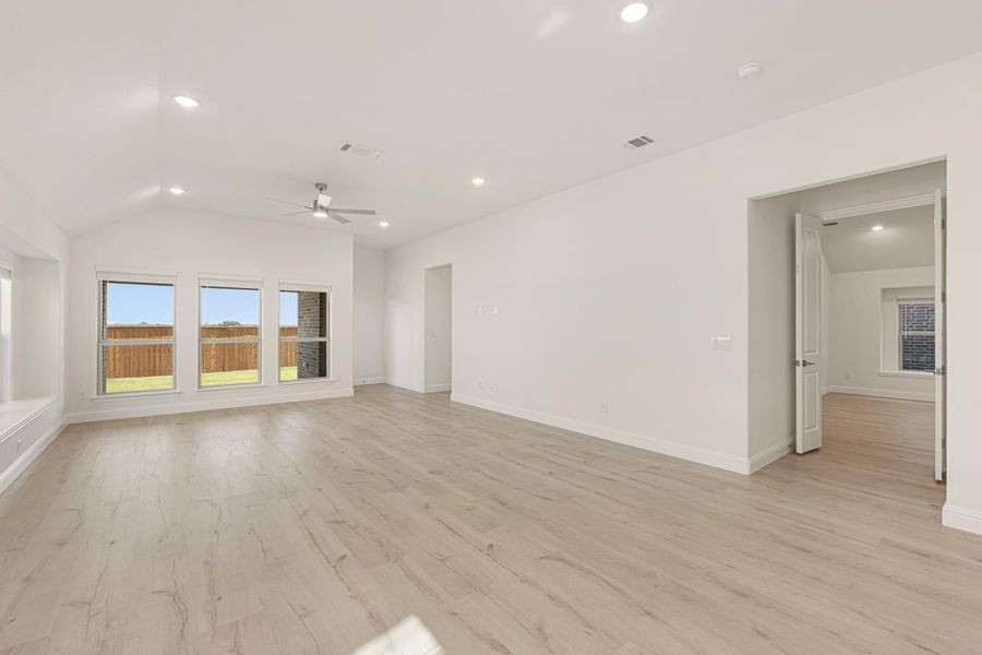 Open living room with vaulted ceiling, ceiling fan, light wood floors, and backyard windows