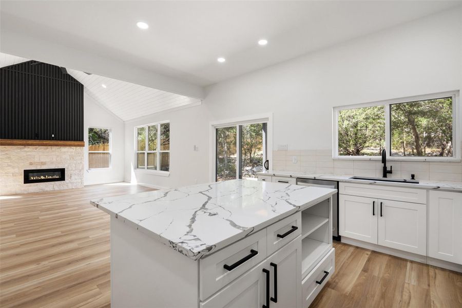 Kitchen with white cabinets, light stone countertops, a center island, light wood-style floors, and tasteful backsplash Kitchen with white cabinets, light stone countertops, a center island, light wood-style floors, and tasteful backsplash