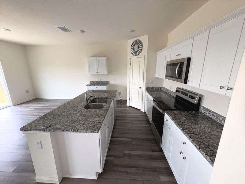 Kitchen featuring appliances with stainless steel finishes, white cabinets, an island with sink, dark stone counters, and dark wood-style floors Kitchen featuring appliances with stainless steel finishes, white cabinets, an island with sink, dark stone counters, and dark wood-style floors