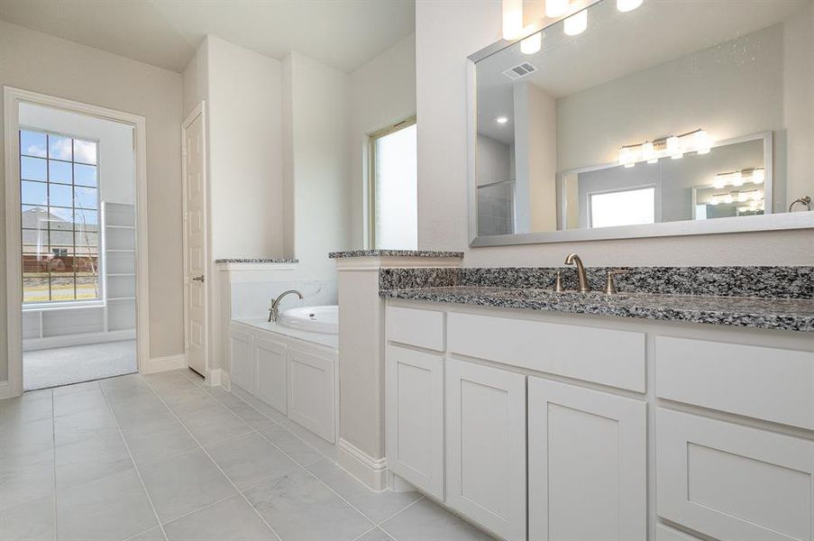 Bathroom with tile patterned flooring, vanity, and a relaxing tiled tub