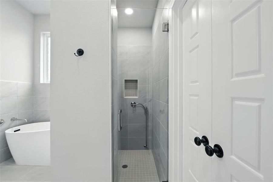 Full bathroom with a stall shower, tile patterned flooring, a freestanding tub, and tile walls Full bathroom with a stall shower, tile patterned flooring, a freestanding tub, and tile walls