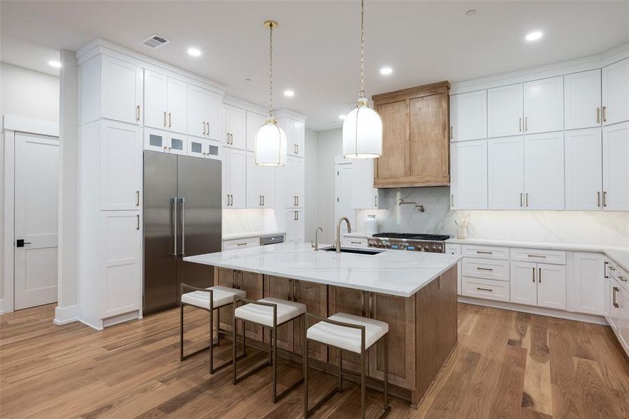 Kitchen with light hardwood / wood-style flooring, decorative backsplash, sink, a center island with sink, and stainless steel built in fridge