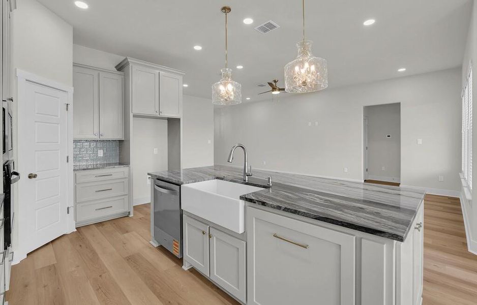 Kitchen with a kitchen island with sink, dark stone countertops, light wood-style flooring, pendant lighting, and backsplash