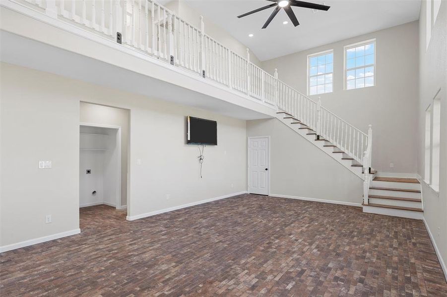 Unfurnished living room featuring a high ceiling, stairs, ceiling fan, and recessed lighting Unfurnished living room featuring a high ceiling, stairs, ceiling fan, and recessed lighting