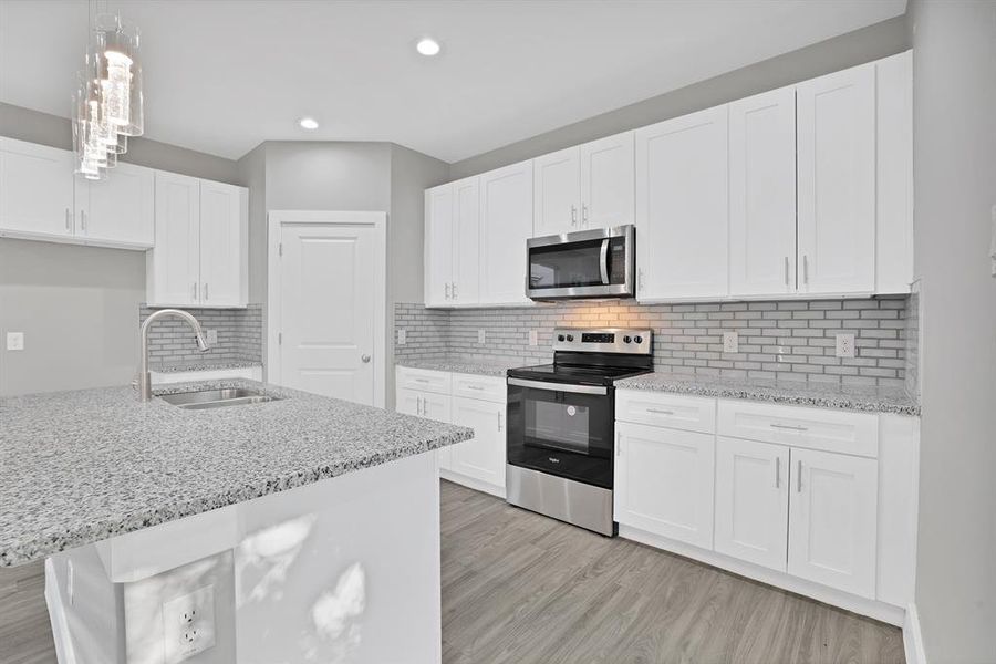 Kitchen featuring stainless steel appliances, sink, light hardwood / wood-style floors, white cabinetry, and hanging light fixtures