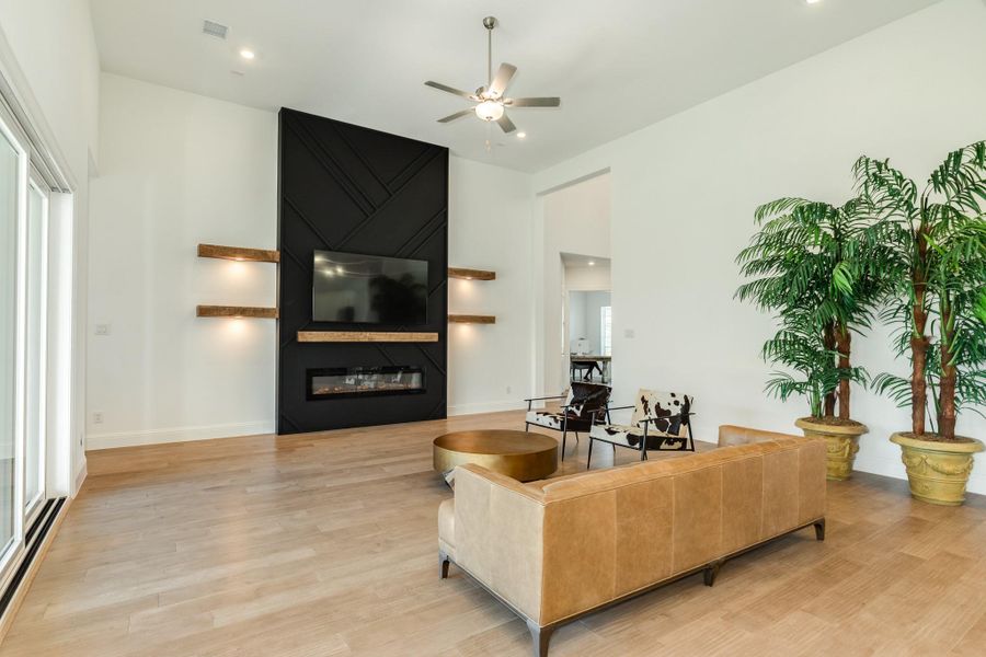 This family room features an elegant, custom-built electric fireplace with adjustable color settings and convenient remote-controlled operation. The space is further enhanced by sophisticated modern side lighting, recessed ceiling fixtures, and impressive high ceilings.
