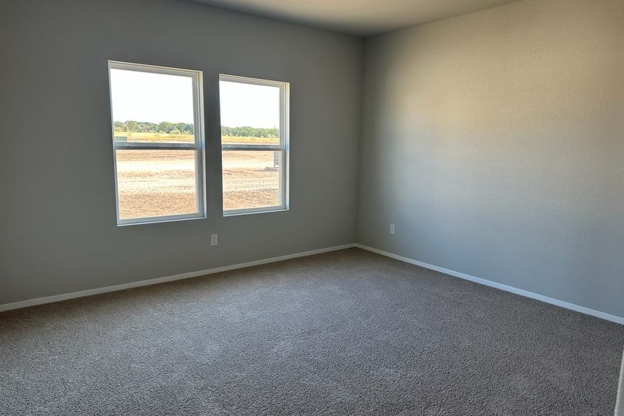 Image of home primary bedroom with light carpet, white walls, and windows