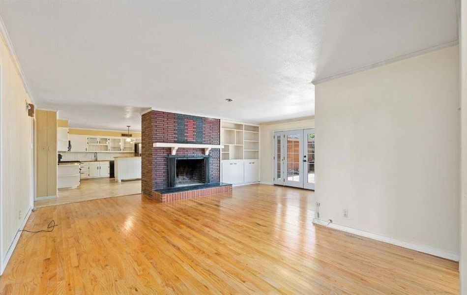 Unfurnished living room featuring a brick fireplace, french doors, light wood-type flooring, built in shelves, and crown molding