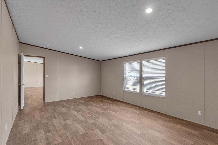 Empty room with a textured ceiling, light wood-type flooring, and crown molding