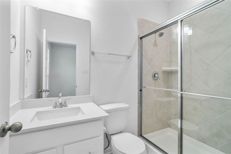 Secondary bath features tile flooring, large walk-in shower with tile surround, stained wood cabinets, beautiful light countertops, mirror, sleek fixtures and modern finishes.