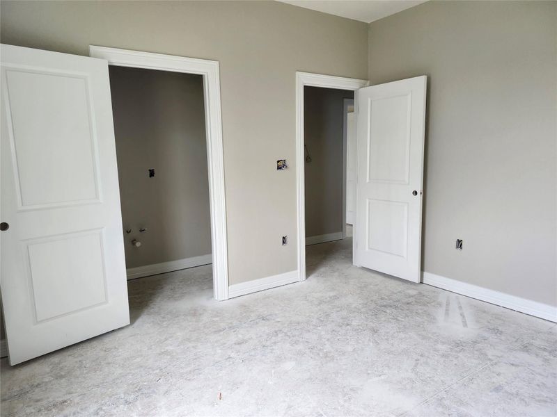 This photo shows a partially finished room with light gray walls, white trim, and two white doors leading to separate areas. The flooring is unfinished, and the room is well-lit, offering a blank canvas for customization.