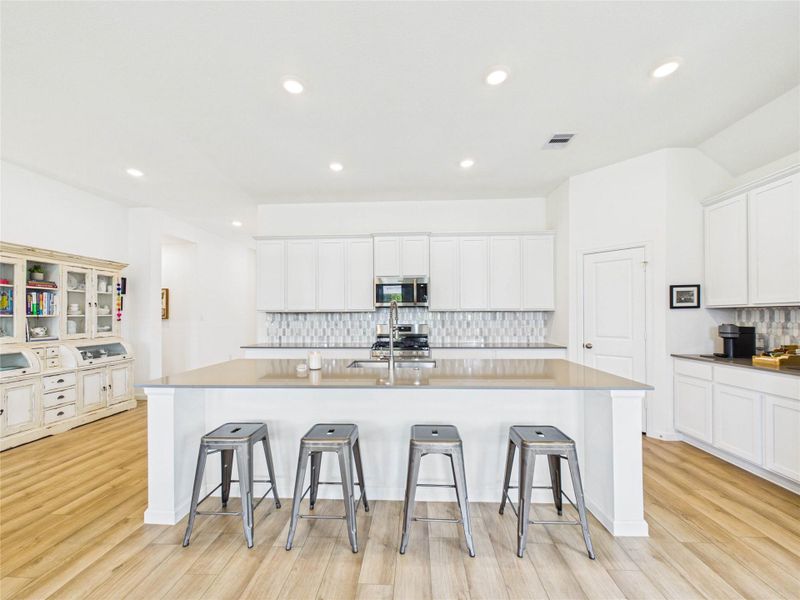The highlight of the kitchen is the oversized island, complete with a sink, dishwasher, and plenty of space for seating. A beautiful tile backsplash adds style and character, while the gas cooktop and oven—with convection and air fry options—create a functional centerpiece for the room. Abundant cabinetry and a spacious walk-in pantry provide excellent storage for everyday living.