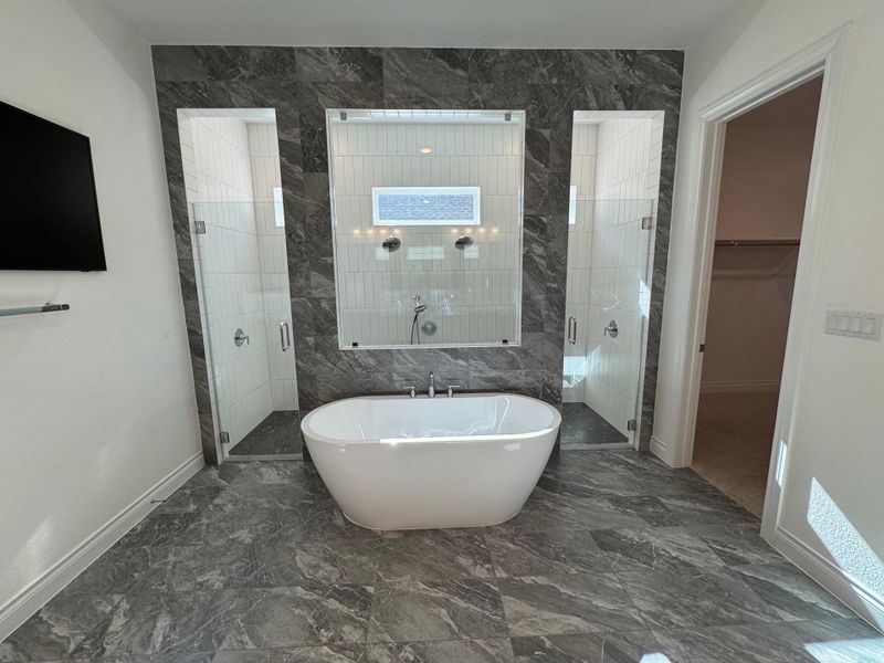 Bathroom featuring a freestanding bath, a spacious closet, a dual head walk in shower, and dark marble finish flooring