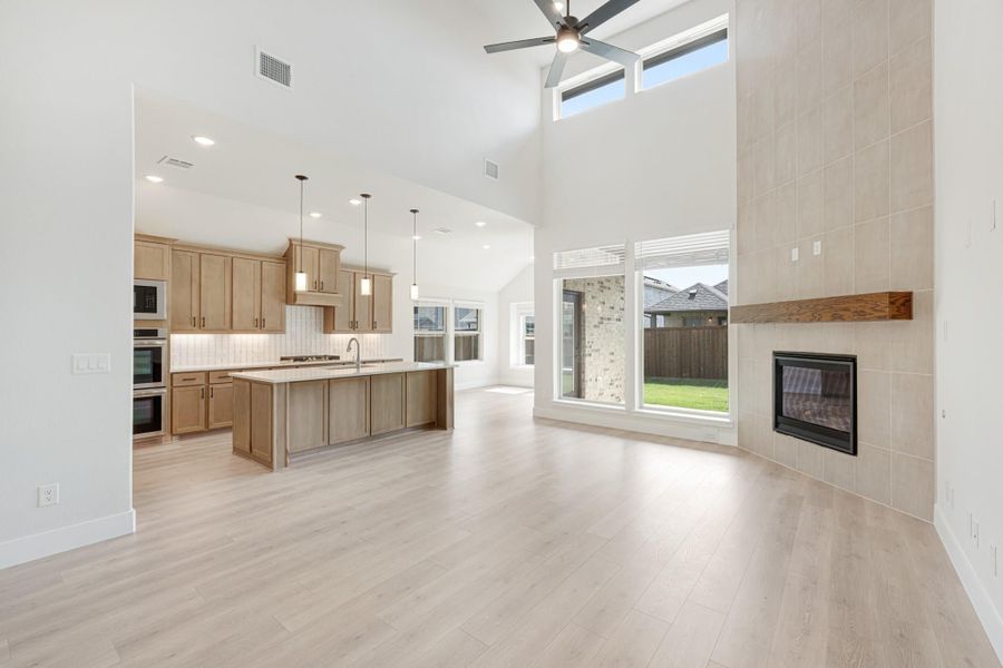 Open-concept living area with tile fireplace, high ceilings, and kitchen with wood cabinets and large island