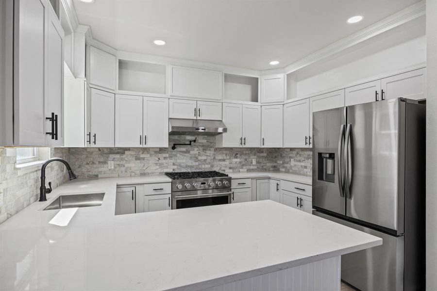 Kitchen with appliances with stainless steel finishes, white cabinetry, light stone countertops, backsplash, and a peninsula Kitchen with appliances with stainless steel finishes, white cabinetry, light stone countertops, backsplash, and a peninsula
