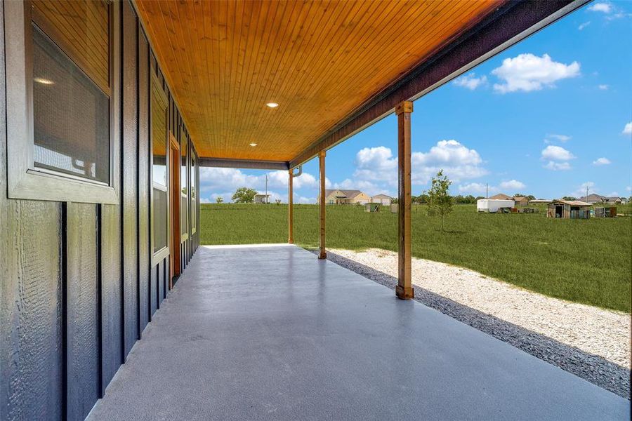 Expansive covered patio with a smooth concrete surface, wood-paneled ceiling, recessed lighting, and exposed timber posts