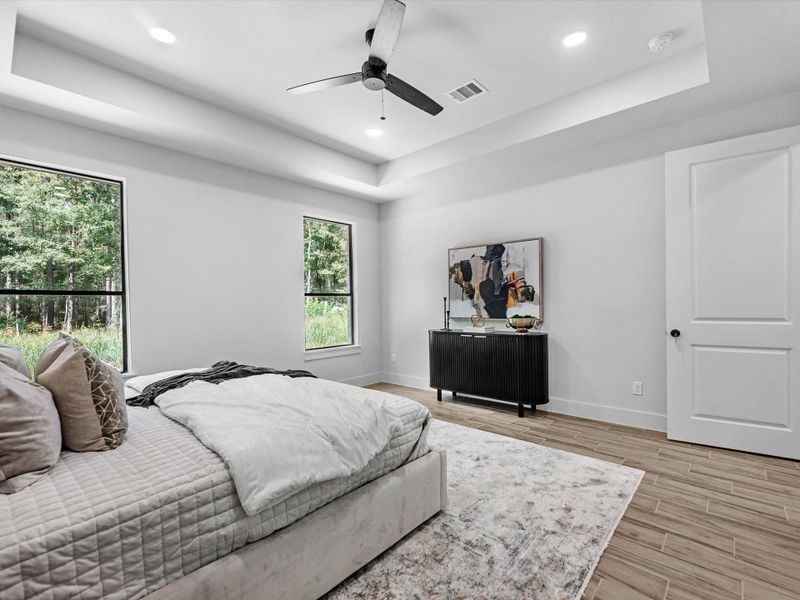 Primary bedroom features; tray ceilings, ceiling fans, backyard views, and tons of space
