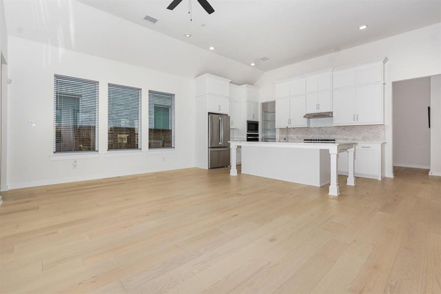 Unfurnished living room with light wood finished floors, vaulted ceiling, ceiling fan, and recessed lighting Unfurnished living room with light wood finished floors, vaulted ceiling, ceiling fan, and recessed lighting