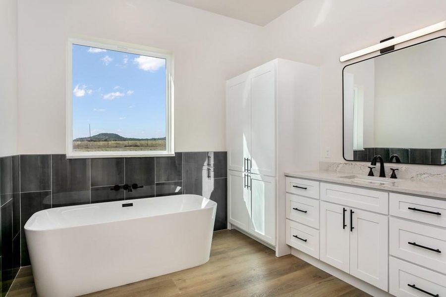 Bathroom with a soaking tub, vanity, light wood-style flooring, and tile walls Bathroom with a soaking tub, vanity, light wood-style flooring, and tile walls