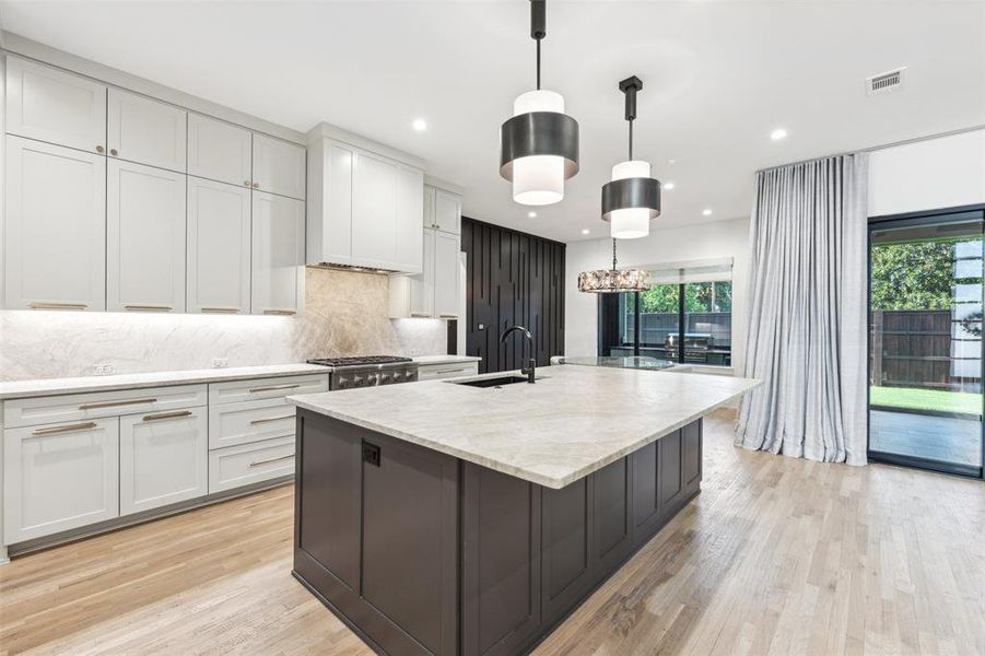 Kitchen featuring sink, decorative backsplash, light wood-type flooring, and a kitchen island with sink