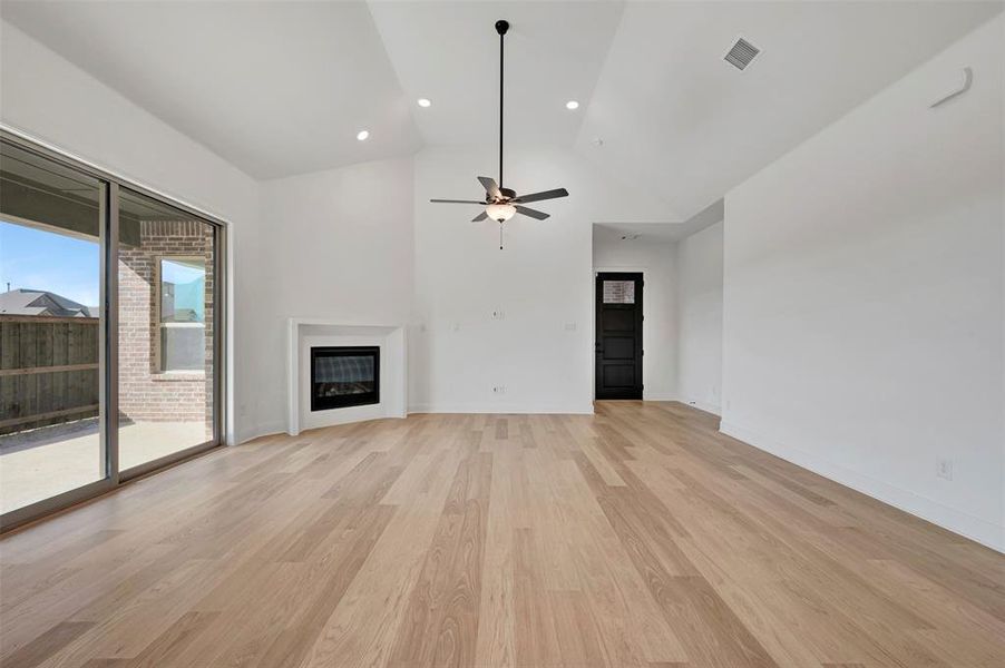 Unfurnished living room with a glass covered fireplace, light wood-type flooring, vaulted ceiling, a ceiling fan, and recessed lighting Unfurnished living room with a glass covered fireplace, light wood-type flooring, vaulted ceiling, a ceiling fan, and recessed lighting