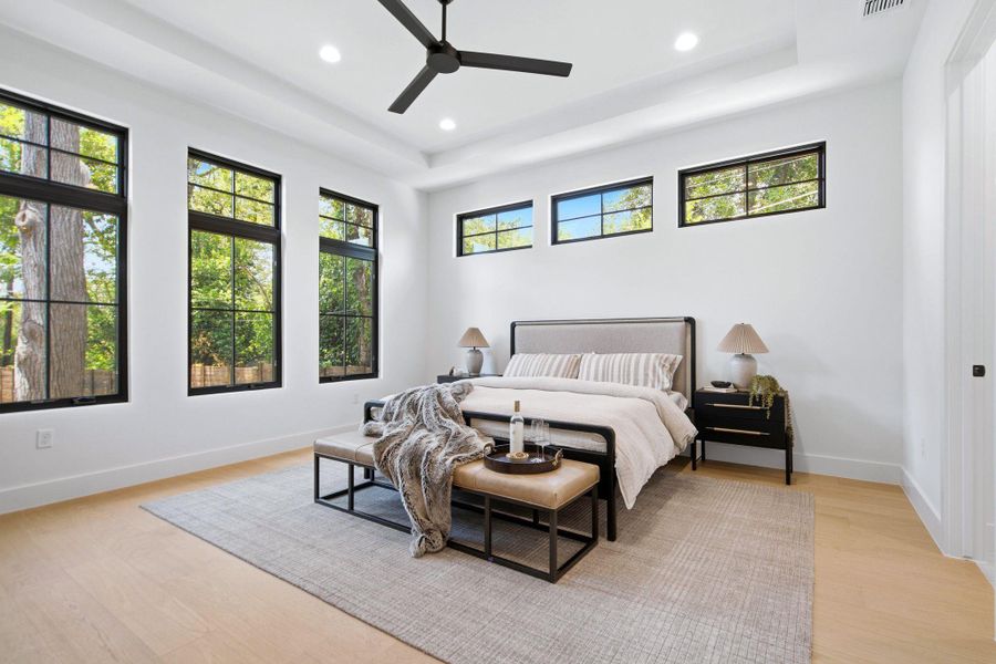Crisp white walls and warm wood flooring define this peaceful bedroom with high tray ceilings.