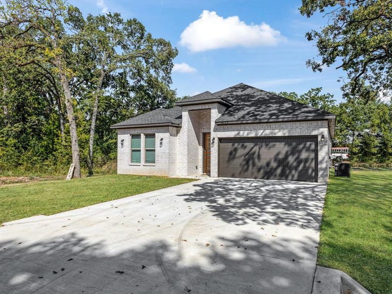 View of front of house with brick siding, concrete driveway, a front yard, a garage, and roof with shingles