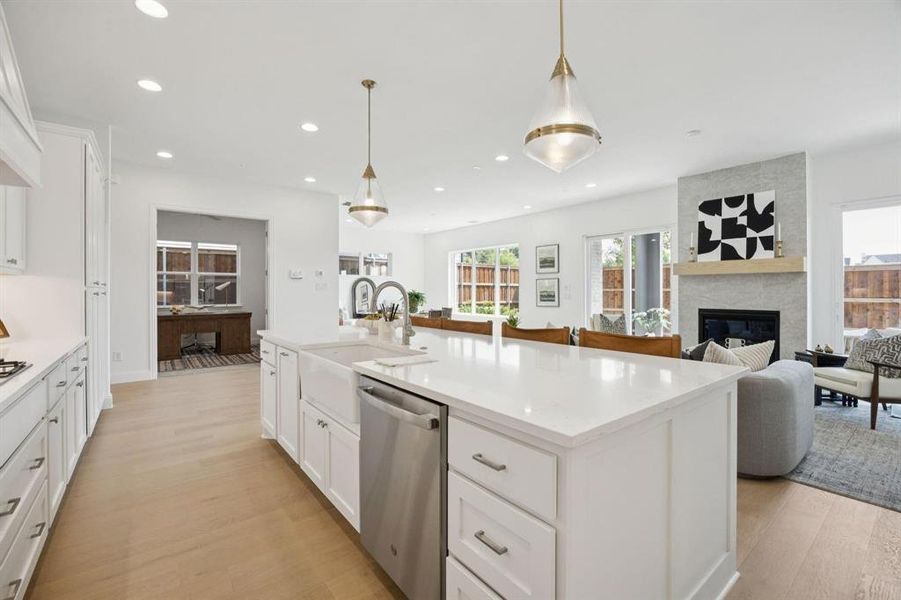Spacious kitchen featuring a large central island with a farmhouse sink and pendant lighting, white cabinetry, integrated stainless steel appliances, and wood-finish flooring