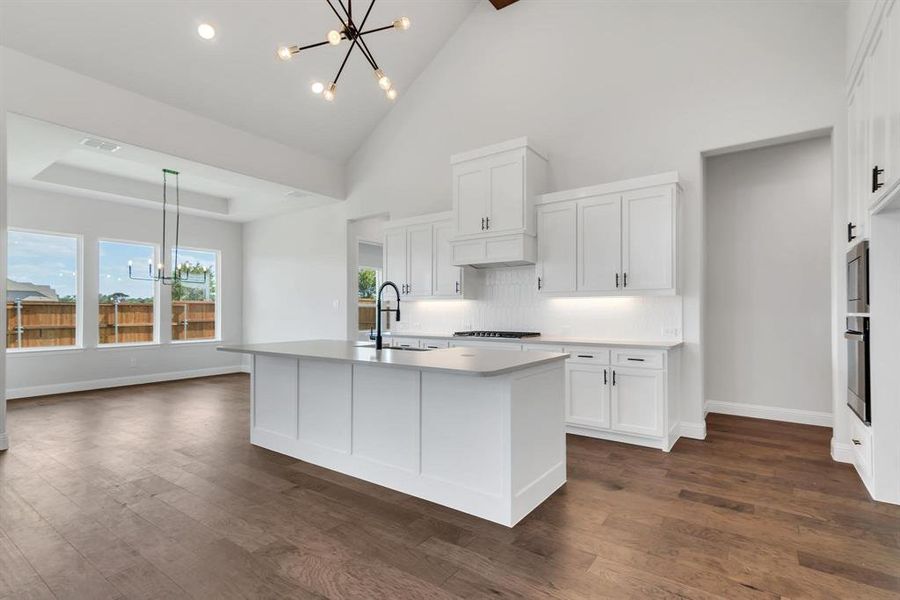 Kitchen with dark hardwood / wood-style floors, white cabinetry, a notable chandelier, and a center island with sink