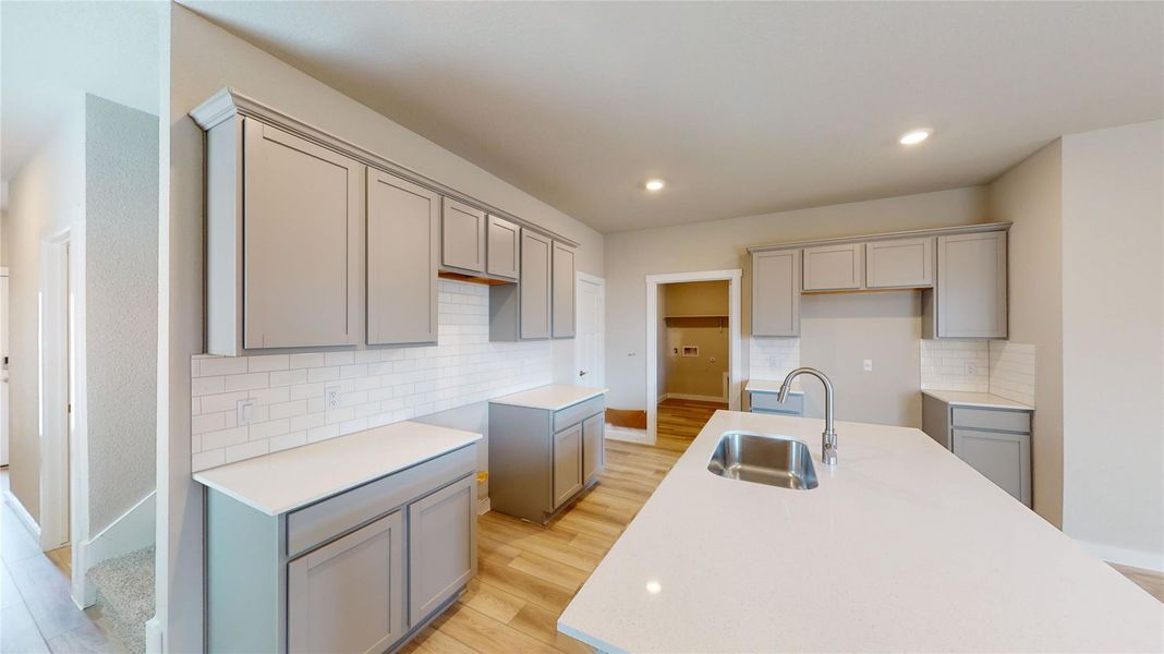 Kitchen featuring light wood-style floors, gray cabinetry, recessed lighting, decorative backsplash, and an island with sink