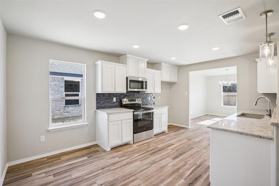 Kitchen featuring stainless steel appliances, light stone counters, white cabinetry, backsplash, and light wood-type flooring