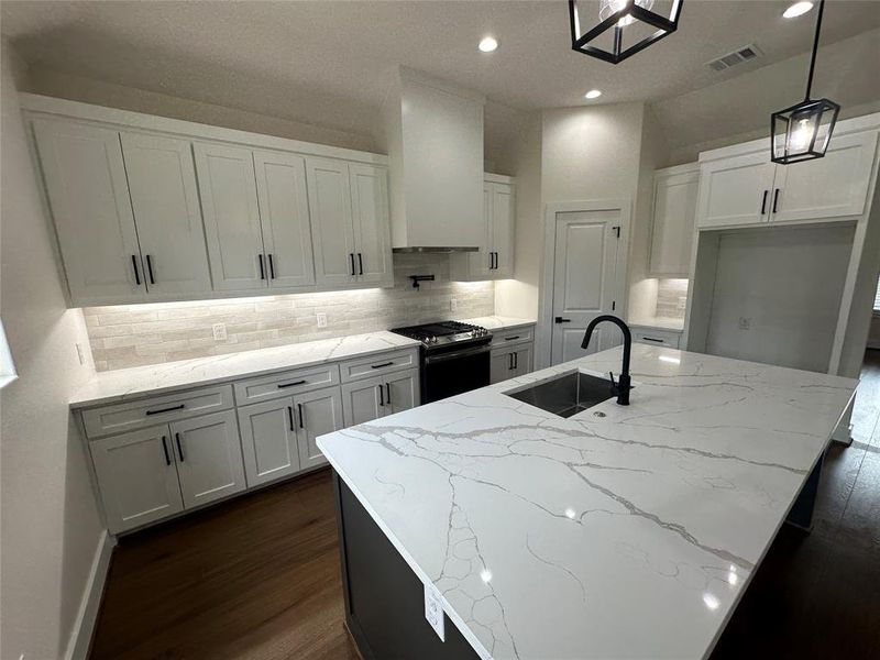 Kitchen featuring range with gas cooktop, a center island with sink, sink, white cabinetry, and dark hardwood / wood-style flooring