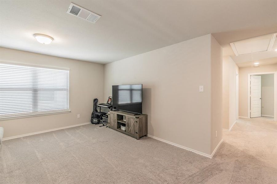 Unfurnished living room with attic access and light carpet