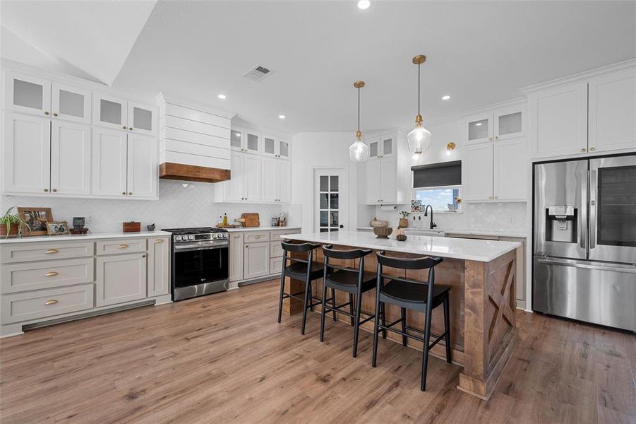 Kitchen featuring appliances with stainless steel finishes, glass insert cabinets, a center island, a breakfast bar area, and tasteful backsplash