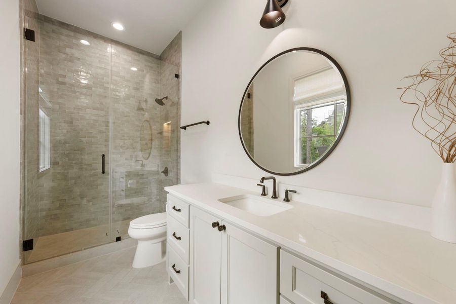 Refined downstairs secondary bathroom with a walk-in glass shower accented by designer tile, complemented by a vanity with stone countertops and contemporary fixtures.