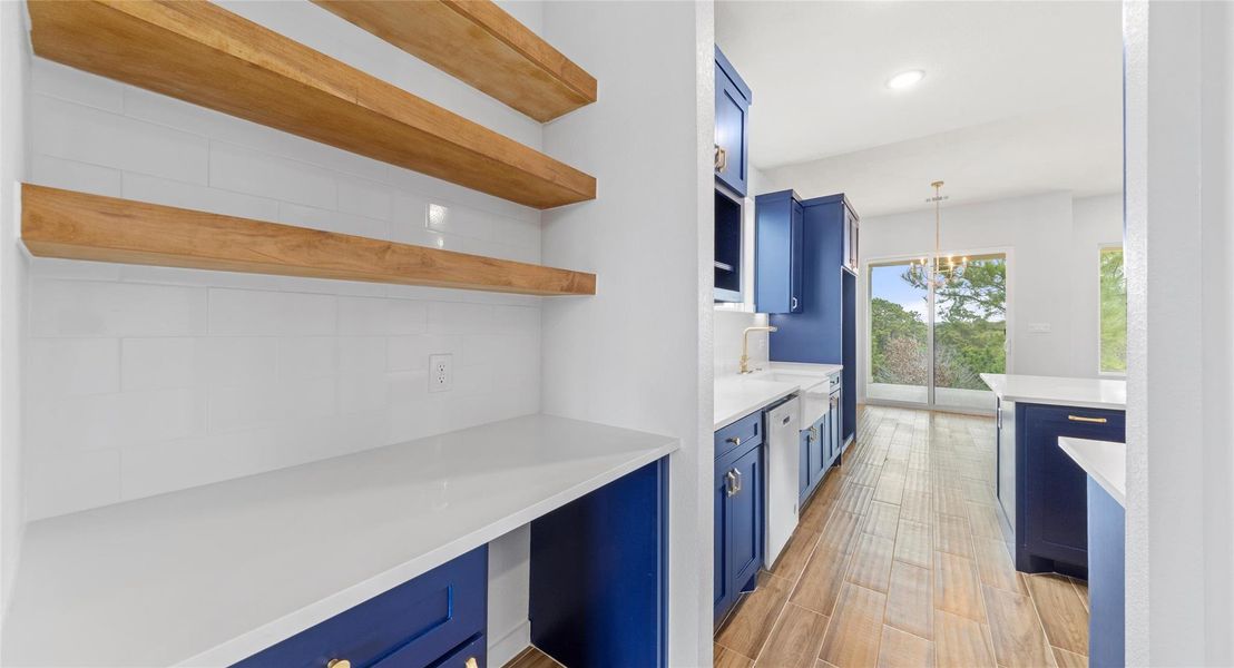 Kitchen featuring blue cabinets, open shelves, decorative light fixtures, light stone counters, and light wood finished floors