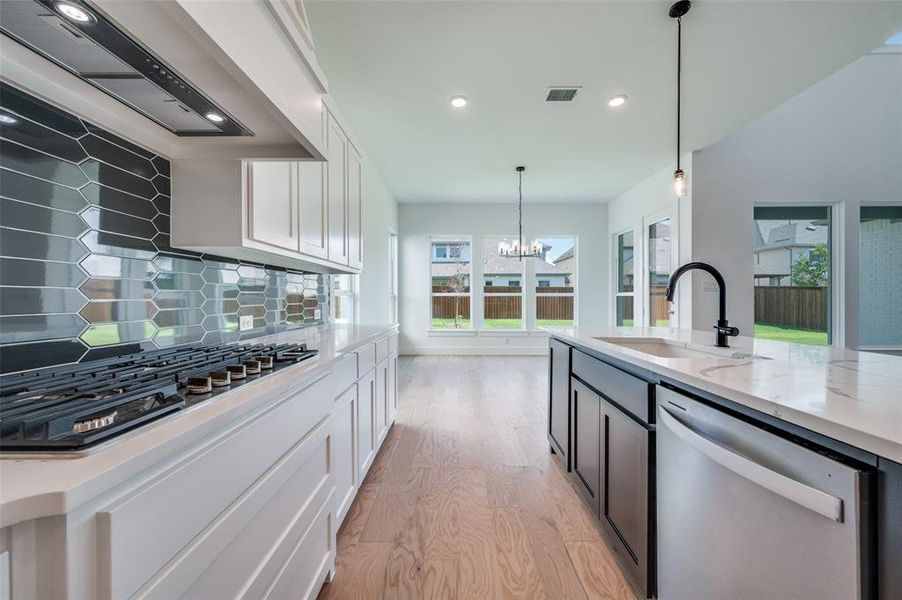 Kitchen featuring custom range hood, tasteful backsplash, dishwasher, light hardwood / wood-style floors, and sink