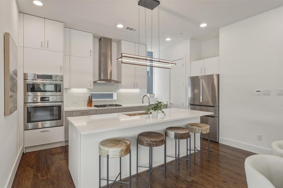 Kitchen with white cabinetry, stainless steel appliances, a kitchen breakfast bar, pendant lighting, and an island with sink
