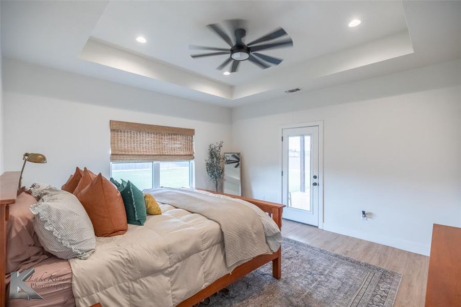 Bedroom featuring wood finished floors, a raised ceiling, multiple windows, and recessed lighting Bedroom featuring wood finished floors, a raised ceiling, multiple windows, and recessed lighting