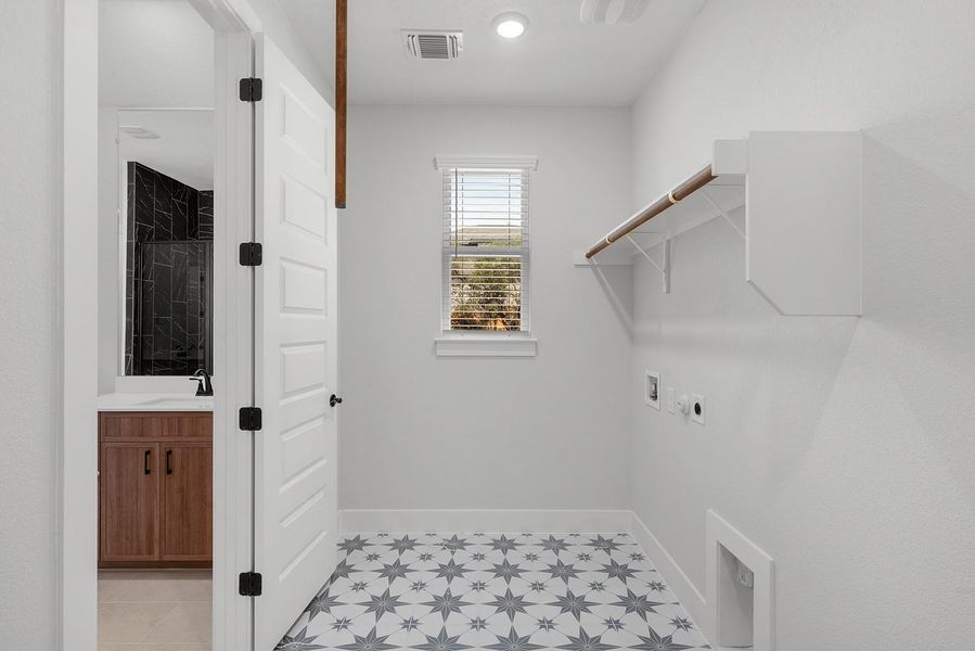 A neatly organized laundry area, featuring patterned flooring and ample shelving, adjoins a bathroom with a sleek vanity.