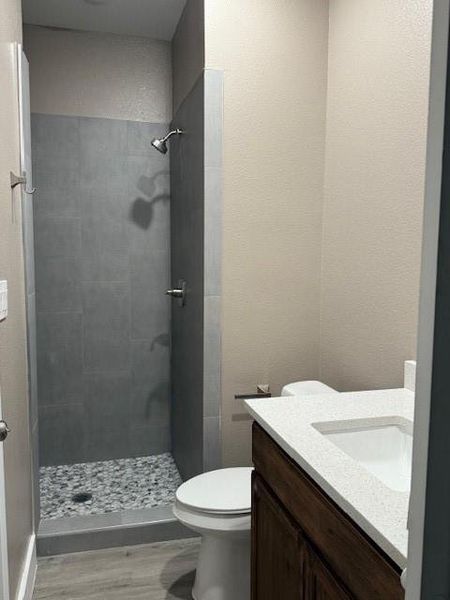 Full bath with toilet, a stall shower, vanity, and wood finished floors