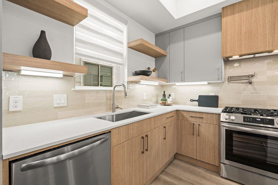 Floating shelves, stainless steel appliances, and under-cabinet lighting introduce warmth, texture, and visual balance throughout the kitchen.