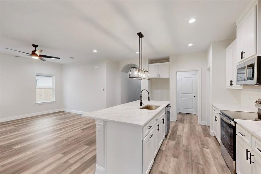 Kitchen featuring sink, stainless steel appliances, white cabinets, and a center island with sink