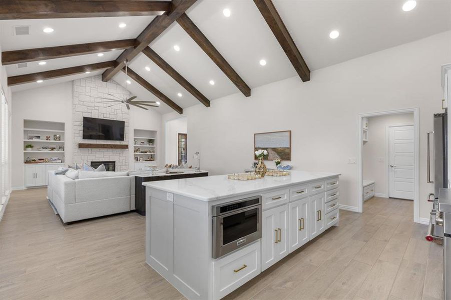 Kitchen featuring light wood-type flooring, a stone fireplace, open floor plan, high vaulted ceiling, and white cabinets Kitchen featuring light wood-type flooring, a stone fireplace, open floor plan, high vaulted ceiling, and white cabinets