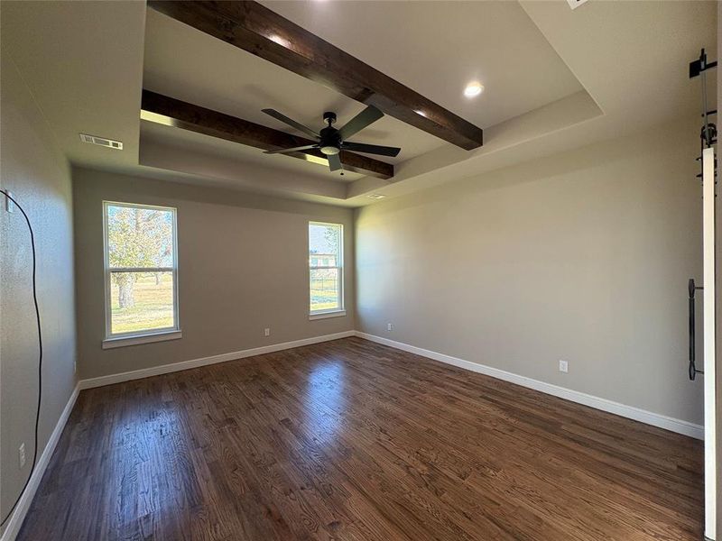 Unfurnished room featuring beamed ceiling, dark wood-type flooring, ceiling fan, and a barn door