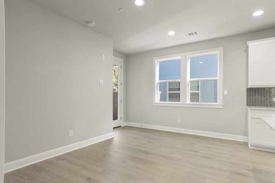 Image of a two story home dining room with light brown flooring and light grey painted walls with a large window