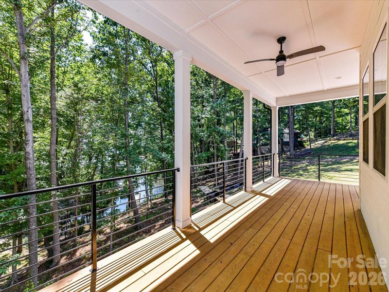 Lakefront covered deck with modern cable railing and ceiling fan, offering peaceful wooded views and the perfect setting to relax and enjoy waterfront living.