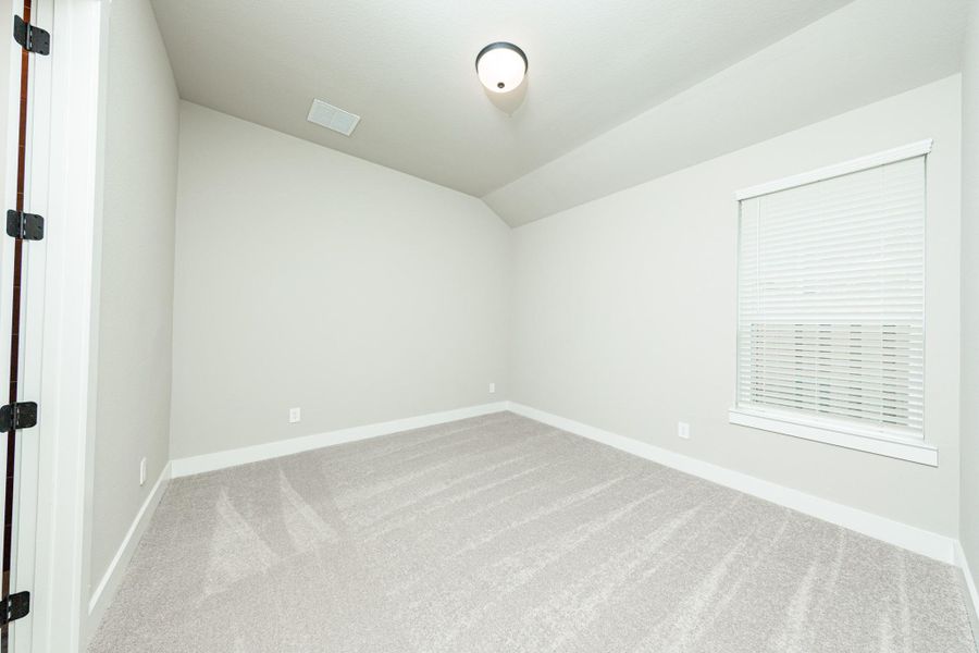 This secondary bedroom features a sloped ceiling, plush carpet flooring, a large window, a walk-in closet, and an ensuite secondary bathroom.
