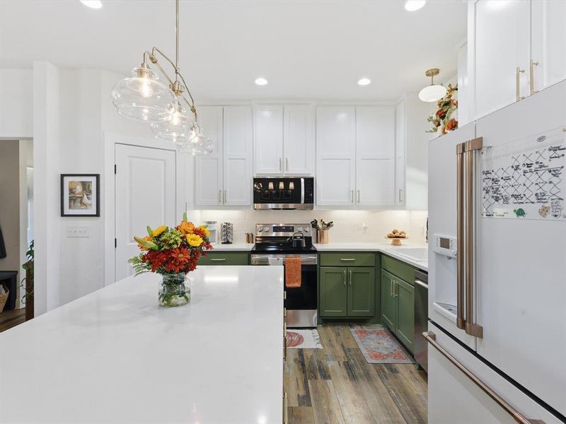Kitchen featuring appliances with stainless steel finishes, green cabinets, decorative backsplash, white cabinetry, and decorative light fixtures