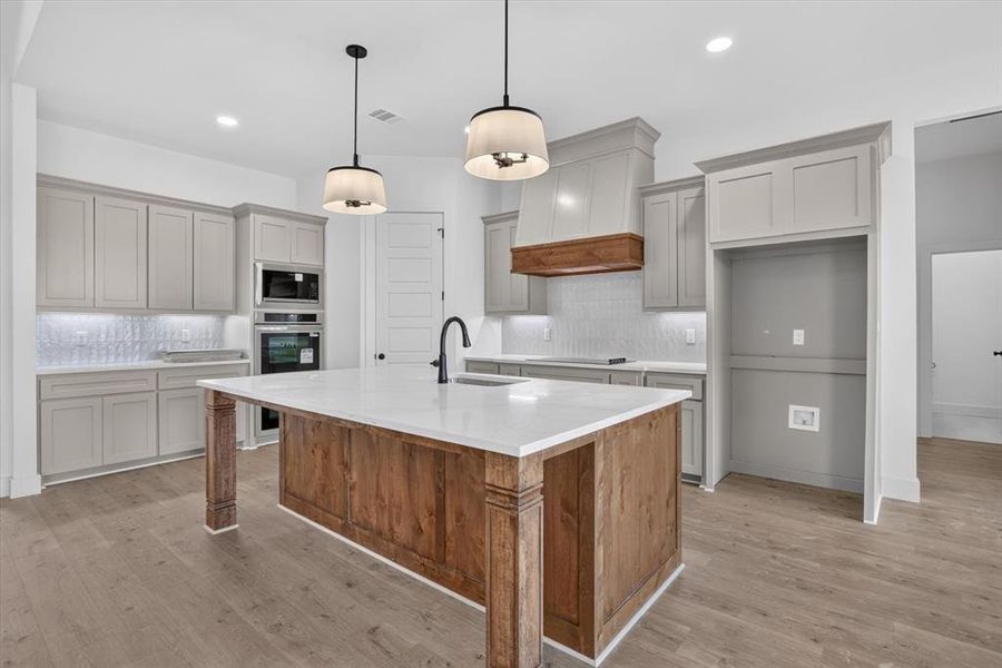 Kitchen featuring a wood-finish island with a white countertop, light gray cabinetry, built-in stainless steel appliances, and wood-finish flooring Kitchen featuring a wood-finish island with a white countertop, light gray cabinetry, built-in stainless steel appliances, and wood-finish flooring